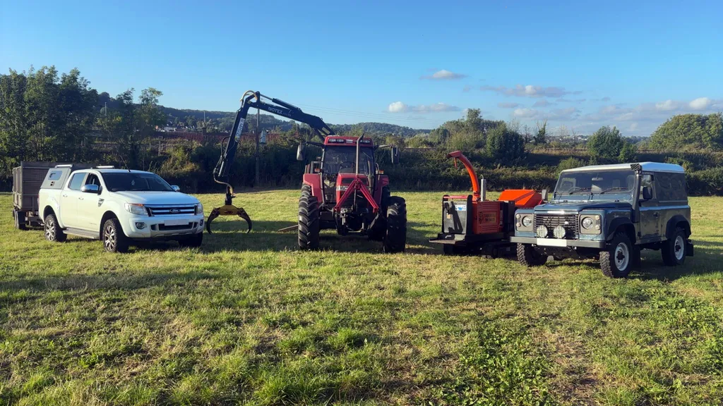 The HGM Contracting fleet parked in a field: pickup and trailer, tractor with timber crane and grapple, wood chipper and Land Rover